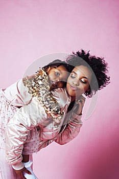 Young pretty african-american mother with little cute daughter hugging, happy smiling on pink background, lifestyle