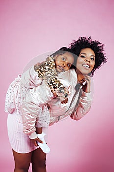 Young pretty african-american mother with little cute daughter hugging, happy smiling on pink background, lifestyle