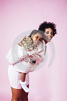 Young pretty african-american mother with little cute daughter hugging, happy smiling on pink background, lifestyle