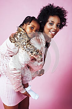 Young pretty african-american mother with little cute daughter hugging, happy smiling on pink background, lifestyle