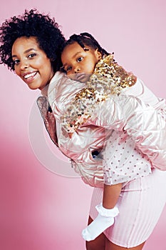 Young pretty african-american mother with little cute daughter hugging, happy smiling on pink background, lifestyle