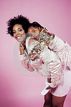 Young pretty african-american mother with little cute daughter hugging, happy smiling on pink background, lifestyle