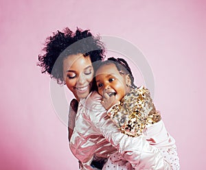 young pretty african-american mother with little cute daughter hugging, happy smiling on pink background, lifestyle