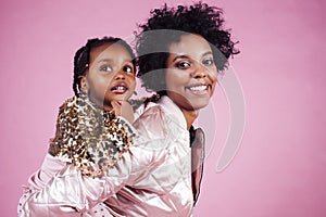 young pretty african-american mother with little cute daughter hugging, happy smiling on pink background, lifestyle