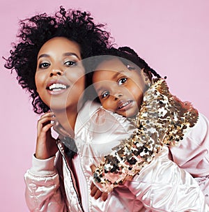 young pretty african-american mother with little cute daughter hugging, happy smiling on pink background, lifestyle