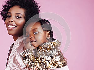 young pretty african-american mother with little cute daughter hugging, happy smiling on pink background, lifestyle