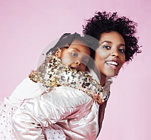 young pretty african-american mother with little cute daughter hugging, happy smiling on pink background, lifestyle