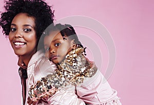 young pretty african-american mother with little cute daughter hugging, happy smiling on pink background, lifestyle