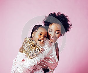 Young pretty african-american mother with little cute daughter hugging, happy smiling on pink background, lifestyle