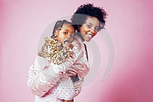 Young pretty african-american mother with little cute daughter hugging, happy smiling on pink background, lifestyle