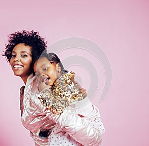 Young pretty african-american mother with little cute daughter hugging, happy smiling on pink background, lifestyle