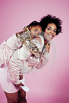 Young pretty african-american mother with little cute daughter hugging, happy smiling on pink background, lifestyle