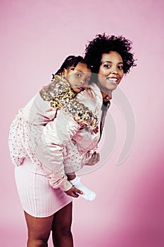 Young pretty african-american mother with little cute daughter hugging, happy smiling on pink background, lifestyle