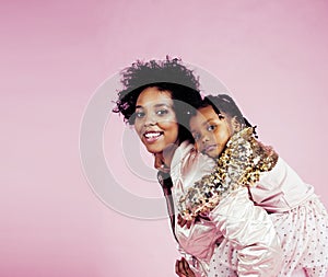 Young pretty african-american mother with little cute daughter hugging, happy smiling on pink background, lifestyle