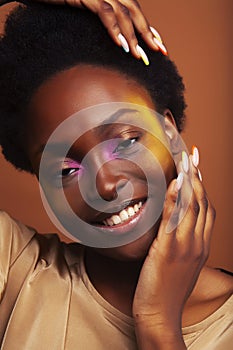 Young pretty african girl with bright colorful makeup and manicure posing cheeful on brown background, lifestyle people