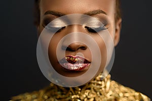 Young pretty african woman, with hair gathered in hairstyle and sensitive gold make-up, posing on black background, in studio, clo