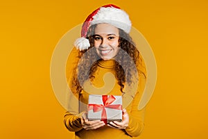 Young pretty african woman smiling, holding gift box on yellow studio background