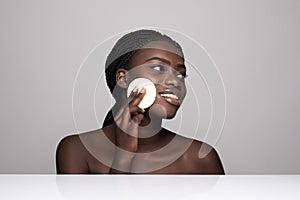 Young pretty afro american woman taking off her makeup with cotton wipe sponge isolated on white background