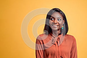 Young pretty afro woman feeling happy, proud and hopeful, wondering or thinking, looking up to copy space. Yellow background