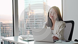 Young pretty Asian business woman sitting in corporate office with laptop.