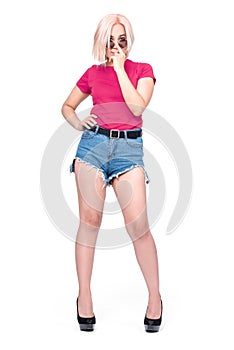 A young pretty Asian girl in a pink T-shirt, denim shorts holds sunglasses on her face with her finger, isolated