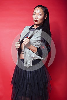 Young pretty asian girl posing cheerful on red background, fashion makeup and clothers