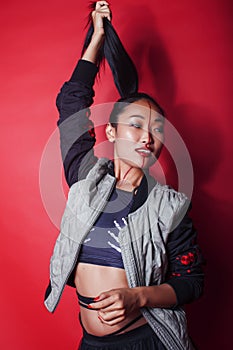 Young pretty asian girl posing cheerful on red background, fashion makeup and clothers