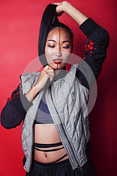 young pretty asian girl posing cheerful on red background, fashion makeup and clothers