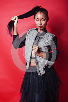 young pretty asian girl posing cheerful on red background, fashion makeup and clothers