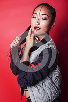 young pretty asian girl posing cheerful on red background, fashion makeup and clothers