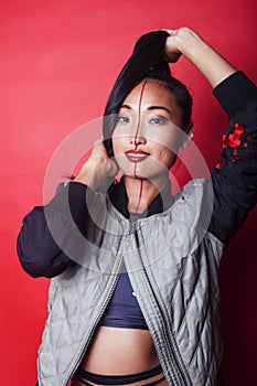 young pretty asian girl posing cheerful on red background, fashion makeup and clothers