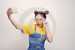 Young pretty Asian girl who wearing a jeans dungaree and yellow glasses, taking selfie, smiling
