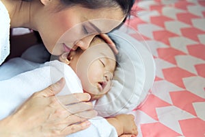 Young pretty Asian mother hugging her sleeping cute baby on the bed. The mother closing her eyes when touching her child softly