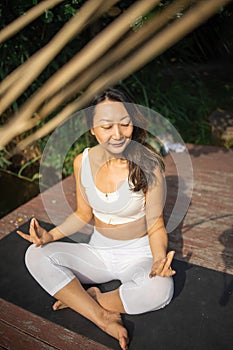Young fit asian woman doing yoga by the lake in the morning park