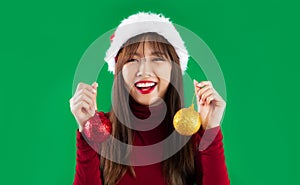 Young pretty asian woman in red sweater wearing santa hat posing smiling and holding red and gold glitter balls