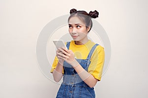 Young pretty Asian woman wearing a jeans dungaree and holding smartphone