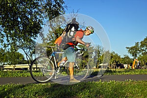 Young pretty athletic man standing with bicycle in colorful summer park.