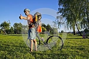 Young pretty athletic man standing with bicycle in colorful summer park.