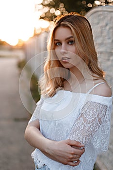 Young pretty attractive woman with blue eyes with natural make-up in an elegant lacy t-shirt posing outdoors near a vintage fence