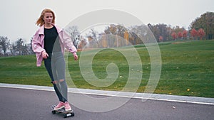 Young pretty beautiful blond hipster woman in pink windstopper having fun riding skateboard longboard downhill on
