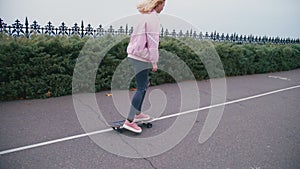 Young pretty beautiful blond hipster woman in pink windstopper having fun riding skateboard longboard downhill on