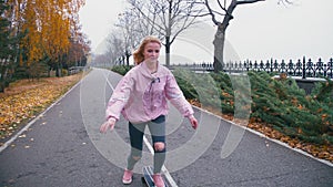 Young pretty beautiful blond hipster woman in pink windstopper having fun riding skateboard longboard downhill on