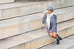 A young pretty black woman is sitting on stairs,  drinking coffee, relaxing