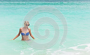 Young pretty blond woman in blue bikini on white tropic beach