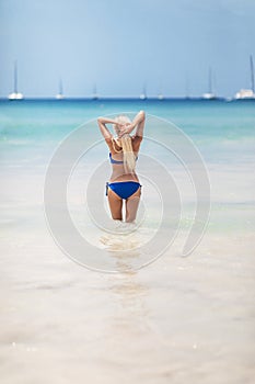 Young pretty blond woman in blue bikini on white tropic beach