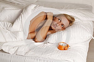 Young pretty blond woman resting in her bed feeling cold with orange alarm clock near her head