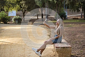 Young, pretty, blonde woman with green eyes, wearing a T-shirt, denim skirt, sitting on a stone bench, taking a picture with her