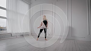 Young pretty blonde woman is rehearsing her dance performance in white dancing hall, jumping and rotating