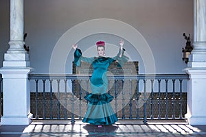 Young, pretty, blonde woman in typical green flamenco suit, doing dancing poses next to a wrought iron railing. Flamenco concept,
