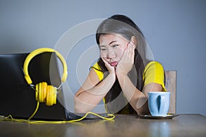 Young pretty and bored Asian Korean student girl working with laptop computer looking unhappy and sleepy holding face with hands